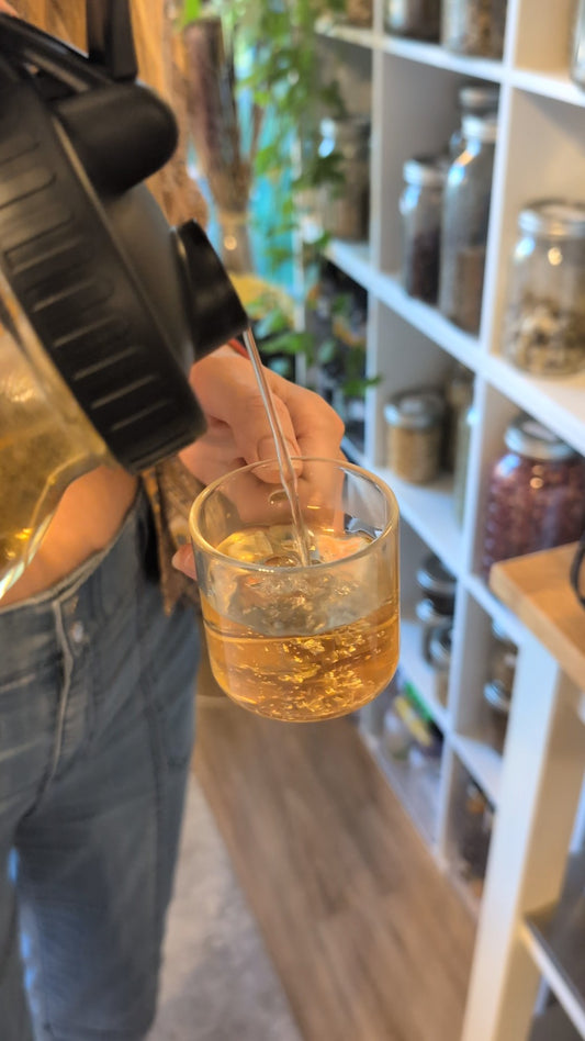 Person holding a glass of amber liquid with a straw in a casual setting.