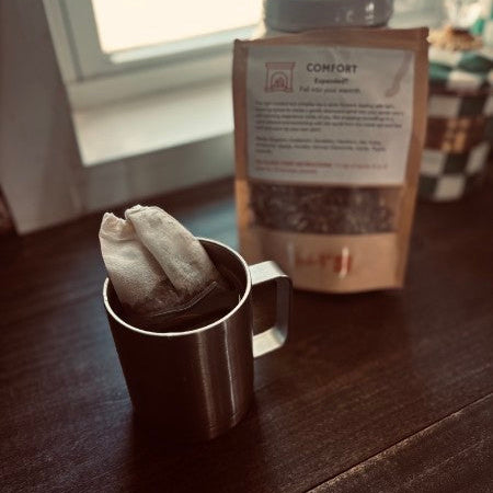 Metal mug with tea bag and a package of loose leaf tea on a wooden surface.