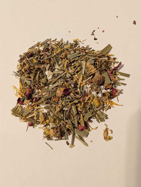 ILLUMINATE herbal tea blend scattered on white background with pops of pink flowers, yellow flowers, and green herbs.